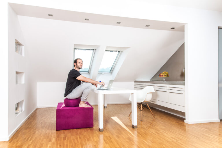 Mann in der assistierten Hocke auf einem paleo chair am Schreibtisch